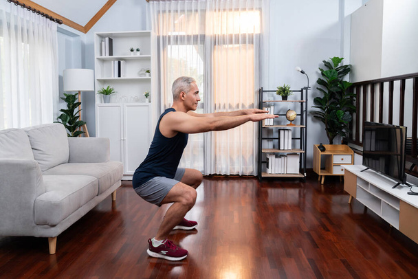 Active and fit senior man warmup and stretching before home exercising routine at living room. Healthy fitness lifestyle concept after retirement for pensioner. Clout - Photo, Image