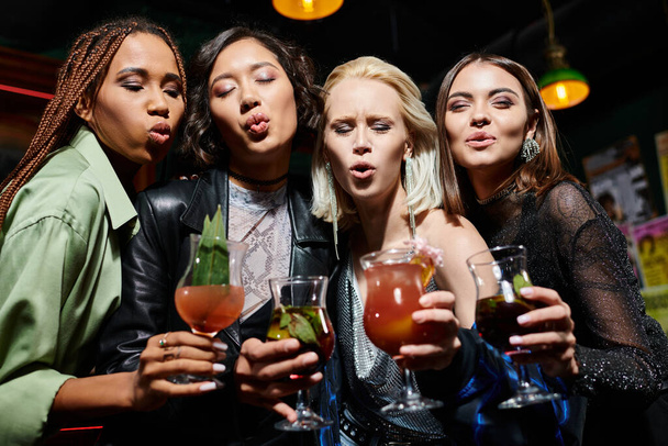glamorosas novias multiétnicas con copas de cóctel haciendo pucheros labios mientras se divierten en el bar - Foto, imagen