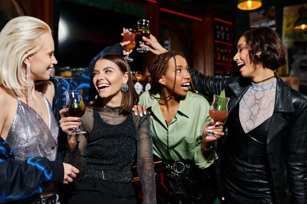 Беззаботные многорасовые девушки звонят в коктейльные бокалы в современном баре, счастье и досуг - Фото, изображение