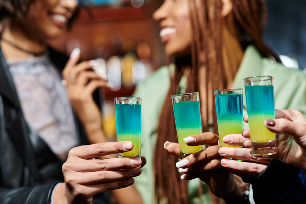 cropped view of blurred multiracial girlfriends holding shot glasses in modern bar, hen party - Photo, Image