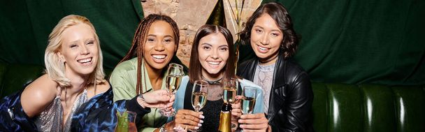 молодые и стильные многонациональные девушки с бокалами для шампанского, улыбающиеся перед камерой в баре, баннер - Фото, изображение