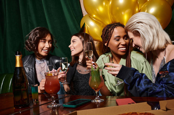 örömteli multiracionális nők ünneplik születésnapját pezsgővel, koktélokkal és arany lufikkal a bárban - Fotó, kép