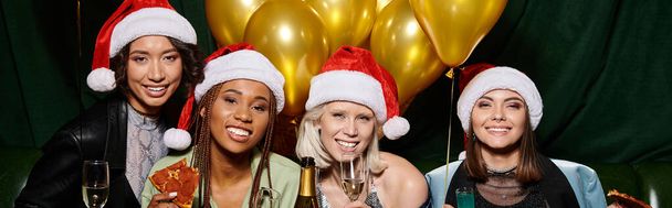 excited multicultural female friends in party hats looking at camera near golden balloons, banner - Photo, Image