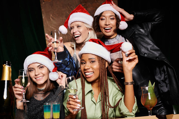 csoport portré izgatott multietnikus barátnők karácsonyi kalap pezsgős poharak a bárban - Fotó, kép