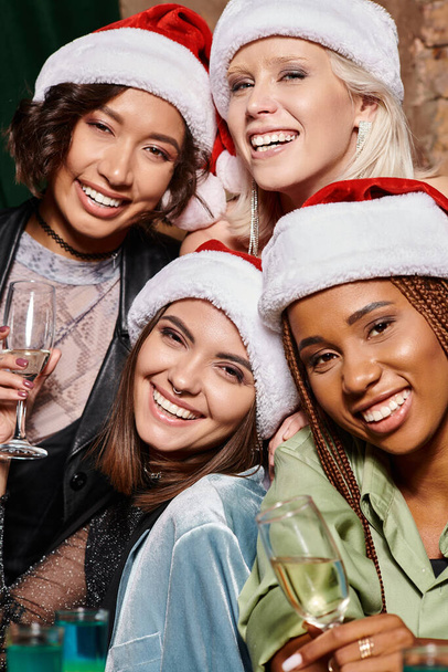 portret van opgewonden multiraciale vrouwen met champagne op zoek naar camera in de bar, kerstfeest - Foto, afbeelding