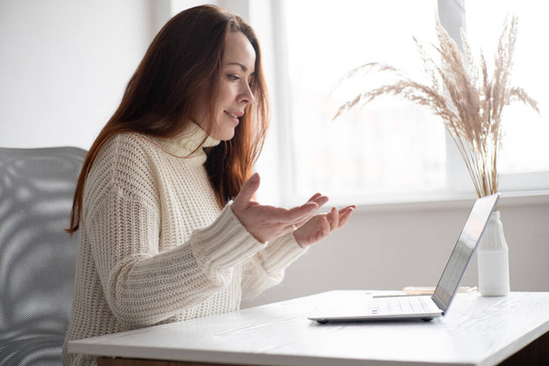 Biała kobieta wykonująca wideo rozmowę z laptopem. Rude włosy kobieta w nowoczesnym biurze - Zdjęcie, obraz