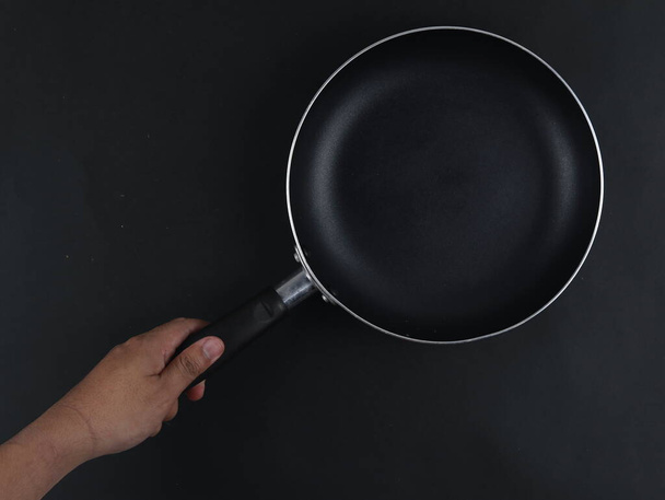 Hand hält Bratpfanne isoliert auf schwarzem Hintergrund - Foto, Bild