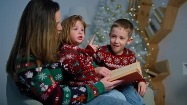 Μια μητέρα διαβάζει μια χριστουγεννιάτικη ιστορία σε παιδιά σε ένα διακοσμημένο δωμάτιο. Μια ευτυχισμένη οικογένεια ετοιμάζεται για τις διακοπές και τα δώρα. Υψηλής ποιότητας 4k πλάνα - Πλάνα, βίντεο