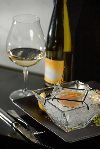Pike fish caviar, na lodzie, z grzankami i masłem, na przezroczystym naczyniu ze szklanką białego wina na ciemnym tle - Zdjęcie, obraz