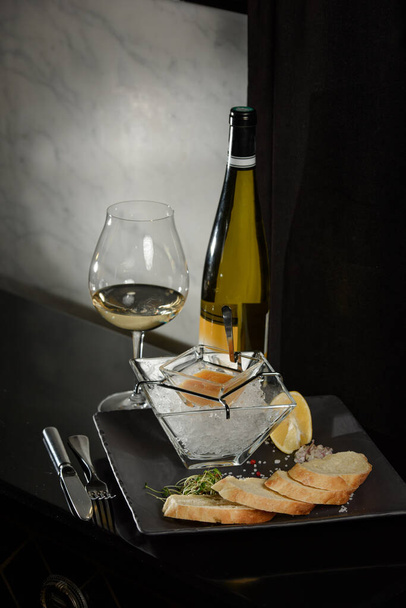 Pike fish caviar, na lodzie, z grzankami i masłem, na przezroczystym naczyniu ze szklanką białego wina na ciemnym tle - Zdjęcie, obraz