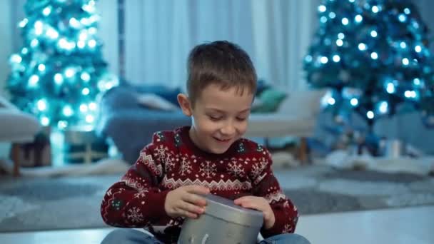 Радісна реліквія: Усміхнений, експресивний хлопчик розв'язує подарунок від Діда Мороза під Святковим ямком. Високоякісні 4k кадри - Кадри, відео