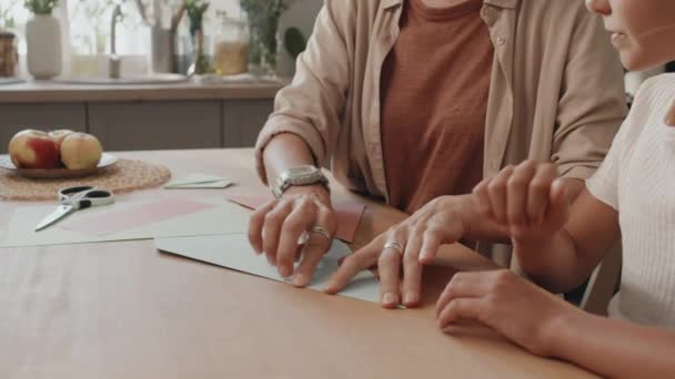 Slow motion selectieve focus portret van moderne moeder en dochter vouwen en snijden van papier tijdens het kijken naar origami tutorial - Video