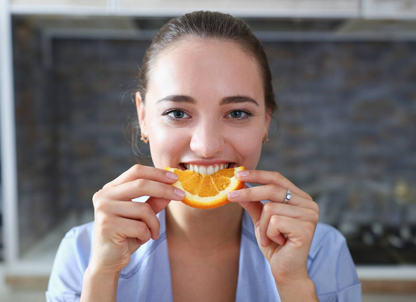 Beautiful brunette smiling woman eat sliced raw tasty orange half at kitchen in the morning portrait. Weight loss beauty fit concept - Photo, Image