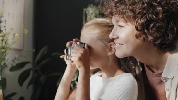 Женщина-фотограф проводит время со своей дочерью дома, обучая ее делать красивые фотографии на камеру - Кадры, видео