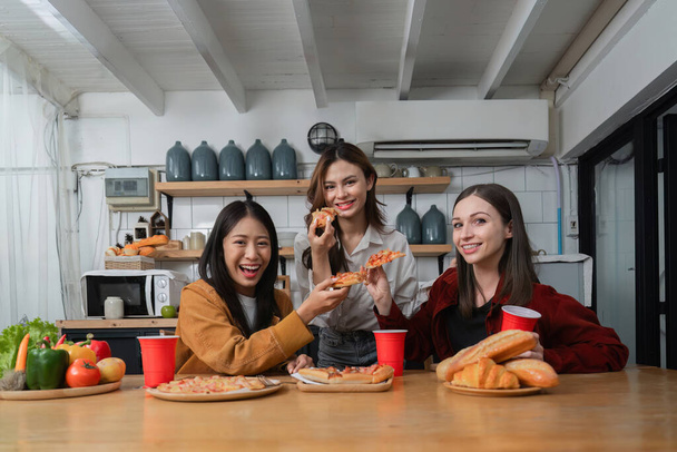 Um grupo de jovens amigas tem uma festa com pizza na mesa e copos vermelhos. Converse e viva juntos felizes, se divertindo em casa.. - Foto, Imagem