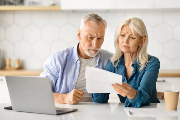 Zdenerwowani małżonkowie w podeszłym wieku sprawdzający dokumenty finansowe przy obliczaniu budżetu rodzinnego w domu, siedząca para starsza przy stole w kuchni, czytająca dokumenty pożyczkowe lub licząca miesięczne wydatki, zbliżenie - Zdjęcie, obraz
