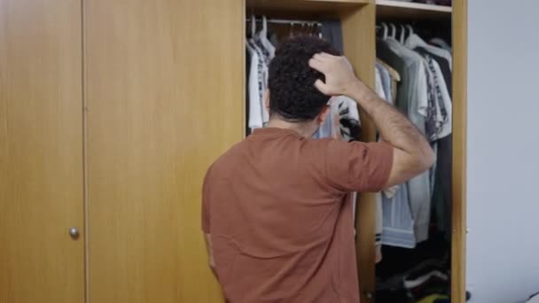 М'язистий латинський хлопець відкриває свій гардероб і дивиться на одяг - 4K Горизонтальне відео - Кадри, відео