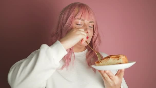 Счастливая молодая веселая женщина носить белую одежду, держа в руке укус кусочек яблочного пирога десерт изолированы на простой пастельно-розовый фон. Правильная концепция здорового питания. Высокое качество - Кадры, видео