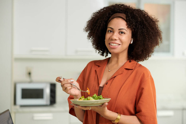 Portret van een lachende vrouw met krullend pluizig haar die tonijnsalade eet als lunch - Foto, afbeelding