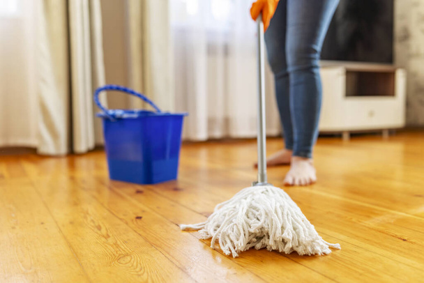 Młoda kobieta w rękawiczkach ochronnych myjąca drewnianą podłogę mopem, odrabiająca pracę domową, rutynowe sprzątanie, koncepcja sprzątania - Zdjęcie, obraz