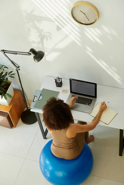 Woman sitting on fitness ball at desk in home office when learning coding - Photo, Image