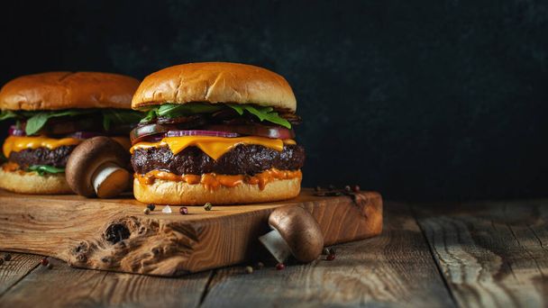 Két ízletes házi hamburger marhahúsból, sajtból és gombából egy régi fából készült asztalon. Dagadt egészségtelen ételek közelről. Fénymásolási hellyel. - Fotó, kép