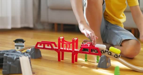 Um rapaz está a brincar com um comboio infantil. A criança brinca com brinquedos de madeira no chão. Um trem de brinquedo cavalga em uma ferrovia de madeira. Imagens 4k de alta qualidade - Filmagem, Vídeo