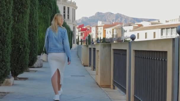 Egy bájos fiatal nő sétál az utcán fordul Mosolygó nő sétál a város központjában élvezi a gyönyörű nap. A ruhás hölgy természetes szépsége az egyik. Kiváló minőségű 4k felvételek - Felvétel, videó