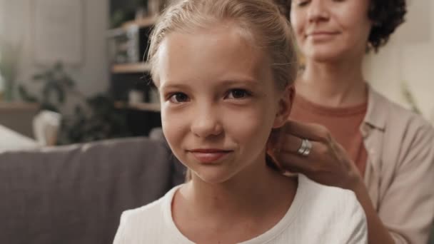 Selektywne zbliżenie ostrości radosnej białej dziewczyny uśmiechniętej do aparatu, podczas gdy matka plecie włosy - Materiał filmowy, wideo