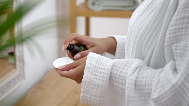 En su baño, una mujer incorpora meticulosamente loción limpiadora en su rutina de cuidado de la piel, usando una almohadilla de algodón cerca del espejo.  - Imágenes, Vídeo