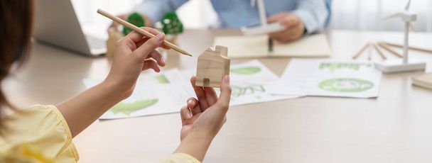 Cropped image of businesswoman presents eco-friendly house by using green design to manager while holding the wooden house block at table with windmill model placed with document. Lehatárolás. - Fotó, kép
