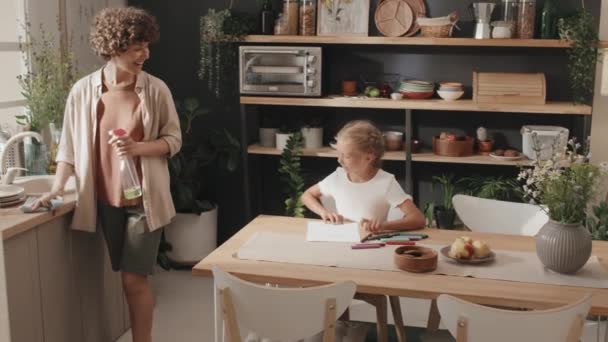 Дівчина сидить за столом у затишній кухні малює картину і показує її мамі, повільний рух - Кадри, відео