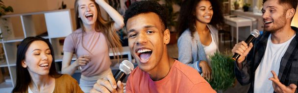 Amusez-vous. Jeune homme enthousiaste chantant avec microphone tout en jouant au karaoké avec des amis dans l'appartement moderne, faisant la fête à la maison. Amitié, concept de loisirs - Photo, image