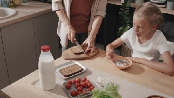Στιγμιότυπο με τη μητέρα να κόβει ψωμί και να φτιάχνει σάντουιτς ενώ η κόρη της τρώει δημητριακά με γάλα - Πλάνα, βίντεο
