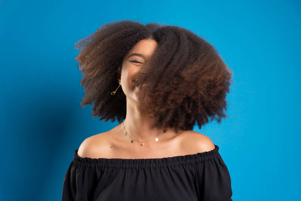 Schöne junge Frau, die mit ihren schwarzen Power-Haaren Bewegungen macht. Vereinzelt auf blauem Hintergrund. - Foto, Bild