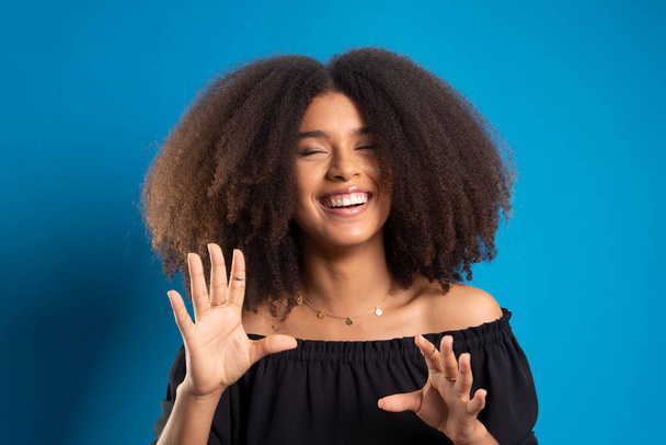 Beautiful young woman with black power hair smiling and looking at the camera. Isolated on blue background. - Photo, Image