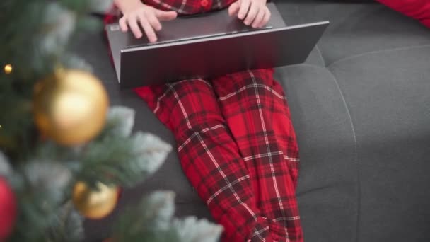 Destejiendo las coloridas bocas del árbol de Navidad, la mujer controla la computadora perfectamente, haciendo pedidos en línea y comunicándose en video con la familia. Imágenes de alta calidad 4k - Metraje, vídeo