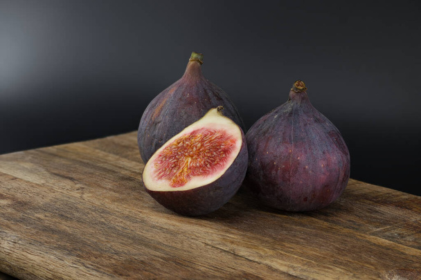 Figs whole and sliced in half on a rustic wooden board over dark background - Photo, Image