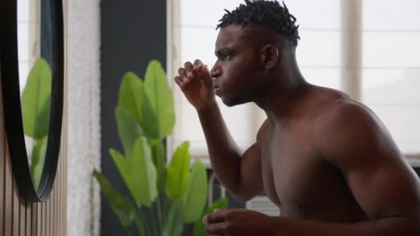 Afro-Américain regardant dans miroir toucher dreadlocks cheveux grossiers bouleversé gars anxieux souffrent de calvitie problème d'alopécie traitement de la peau avec réparation de coiffure produit cosmétique beauté masculine dans la salle de bain - Séquence, vidéo