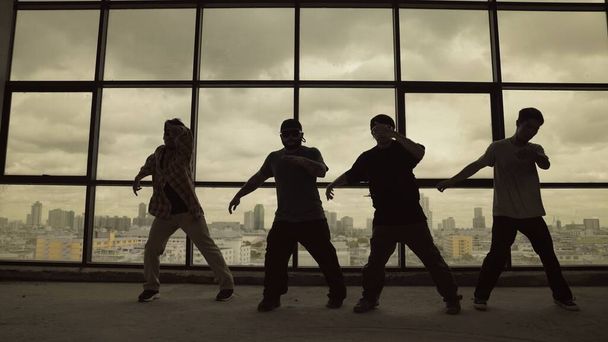 Silhouette felvétel szakképzett koreográfus csoport táncol együtt ég scrapper, városkép háttér. Fiatal hipszter csapat tánc előadás. Szepia szűrő. Árnyék. Kültéri sport 2024. Hatálybalépés. - Fotó, kép