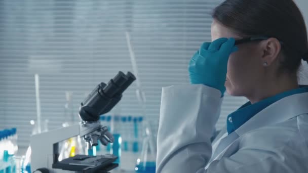 医薬品科学者は新しい薬の安全性と有効性をテストし,大学での医学的実践を改善するのに役立ちます. 顕微鏡の目を通して見た女性,検査 - 映像、動画