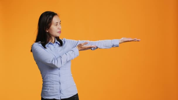 Donna filippina che mostra qualcosa ad entrambi i lati dello studio, presentando pubblicità di marketing sullo sfondo arancione. Giovane adulto che punta a sinistra o a destra per il nuovo annuncio commerciale. - Filmati, video