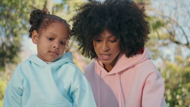Moeder dochter zitten natuur genieten van zonnig weekend samen close-up. Portret van een ontspannen Afro-Amerikaanse vrouw die praat met een schattig klein meisje in Green Park. Zorgeloos gelukkig gezin ontspannen. - Foto, afbeelding