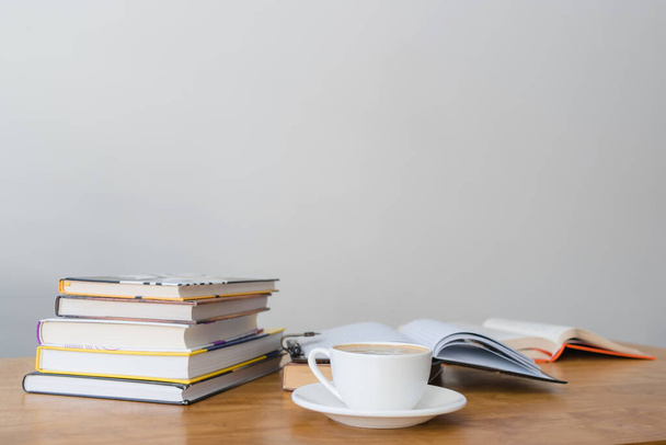 Kopje warme koffie drinken, geopend boek en stapel boeken op houten tafel, focus op de voorgrond. - Foto, afbeelding