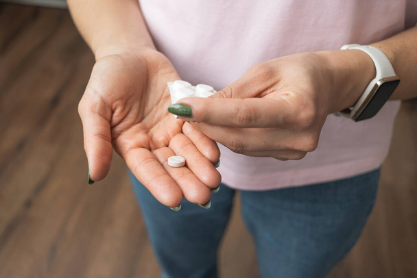 Młoda kobieta trzymająca tabletkę w ręce, środek przeciwbólowy lub antybiotyk, przyjmująca lek z blistra, widok z blistra. - Zdjęcie, obraz