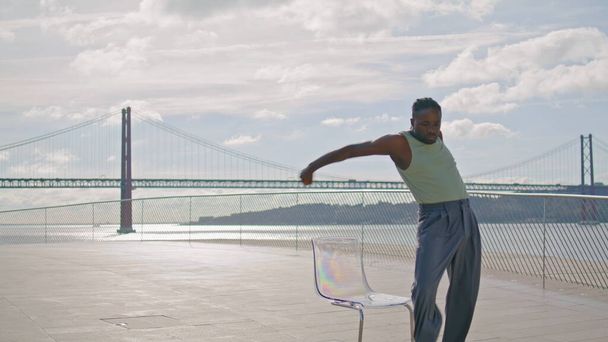 Konzentrierter Typ, der aus Nahaufnahme mit Meerblick tanzt. Afroamerikanische Tänzerin bewegt Körper am Meeresufer Weitschuss. Aktive Männer genießen unterirdischen Lebensstil im städtischen Sommergebiet. Konzept der Subkultur-Bewegung - Foto, Bild