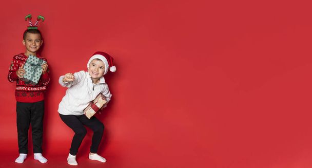 Twee jongens hebben een plezier met kerstcadeaus op rode achtergrond. - Foto, afbeelding
