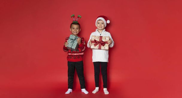 Twee jongens hebben een plezier met kerstcadeaus op rode achtergrond. - Foto, afbeelding