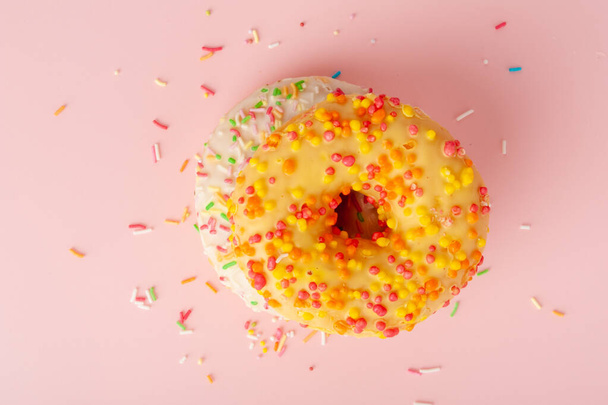 Keltaiset donitsit eristetty, lasitettu himmeä munkkeja värikkäitä strösseleitä, ympyrä kakku donitseja vaaleanpunainen tausta - Valokuva, kuva