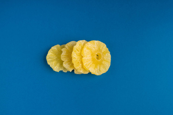 Anelli di ananas secco isolato, ananas caramella, frutta disidratata giallo zucchero, cerchi di frutta canditi, ananas secco su sfondo blu - Foto, immagini